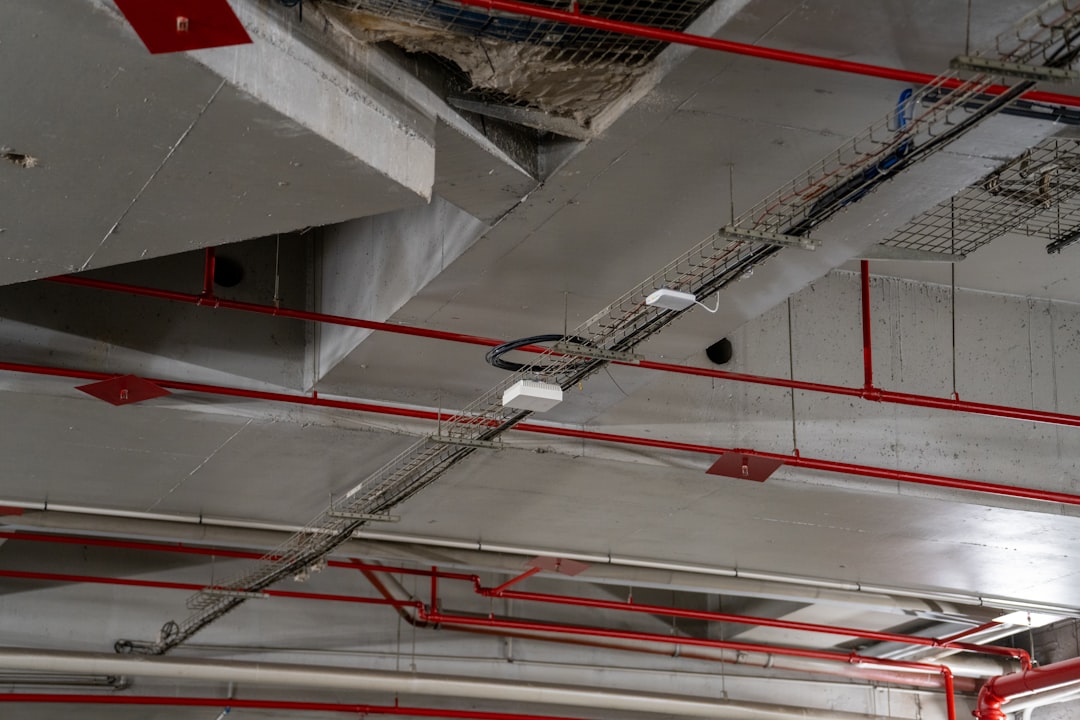 Exposed industrial ceiling with concrete beams, red pipes, and wiring.